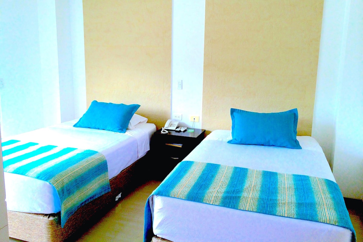 Two single beds with blue pillows and striped blankets, a bedside table with a phone, and a wall socket.