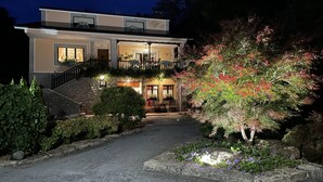 A modern two-story house with a well-lit entrance, a covered porch, and a landscaped garden with a variety of plants and flowers. - Casa Rural Santu Colás (Cangas de Onis)