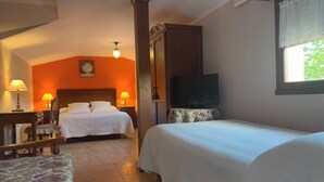 A hotel room with two beds, a desk with a chair, a television, and a window with a view of greenery. - Casa Rural Santu Colás (Cangas de Onis)