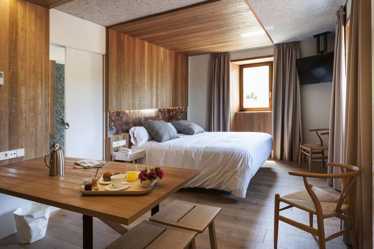 Ett hotellrum med trägolv, en säng med vita sängkläder, ett brickbord med frukost på ett träbord och en tv som är monterad på väggen.