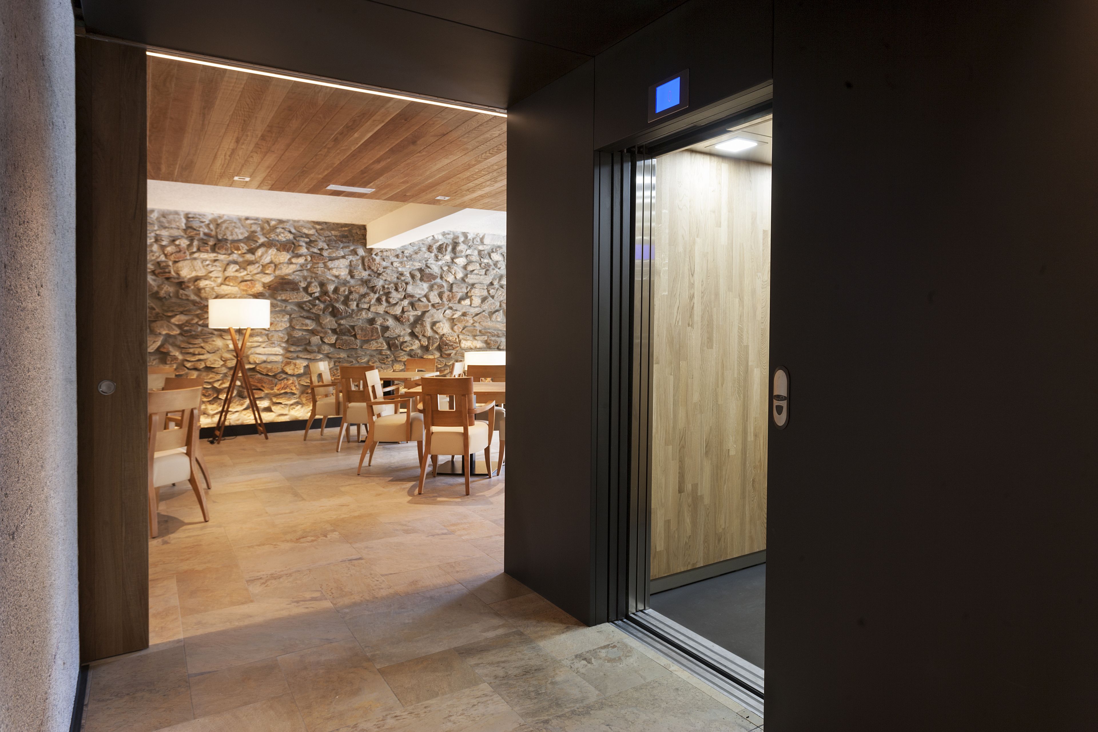 A modern interior with a stone wall, wooden ceiling, and a dining area with chairs and a table.