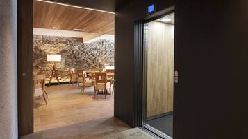 A modern interior with a stone wall, wooden ceiling, and a dining area with chairs and a table.