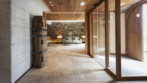 A modern interior with a stone wall, wooden ceiling, and a seating area with a sofa and table. - Palacio de Yrisarri by IrriSarri Land (Igantzi)