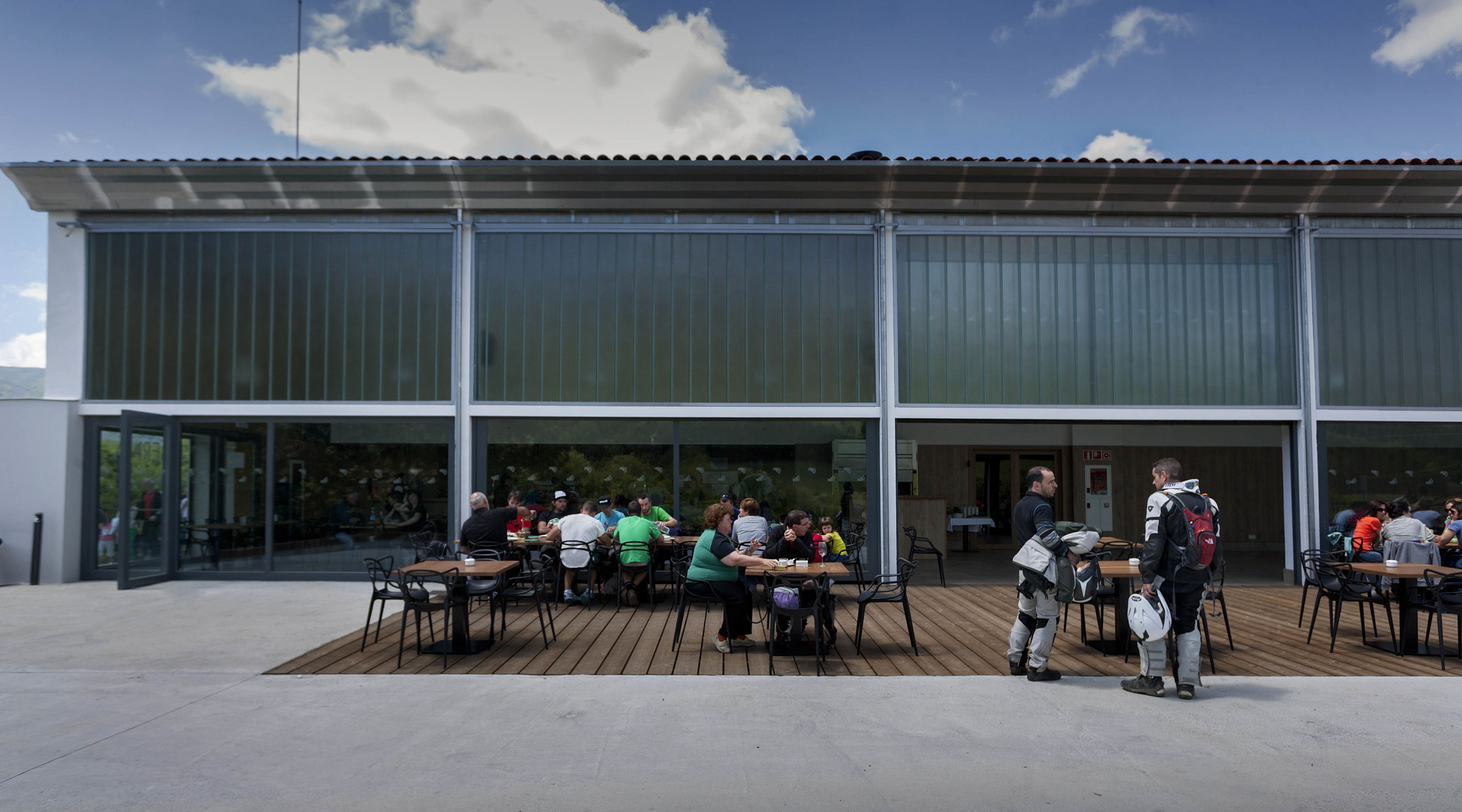 An outdoor dining area with tables and chairs in front of a building with large windows.
