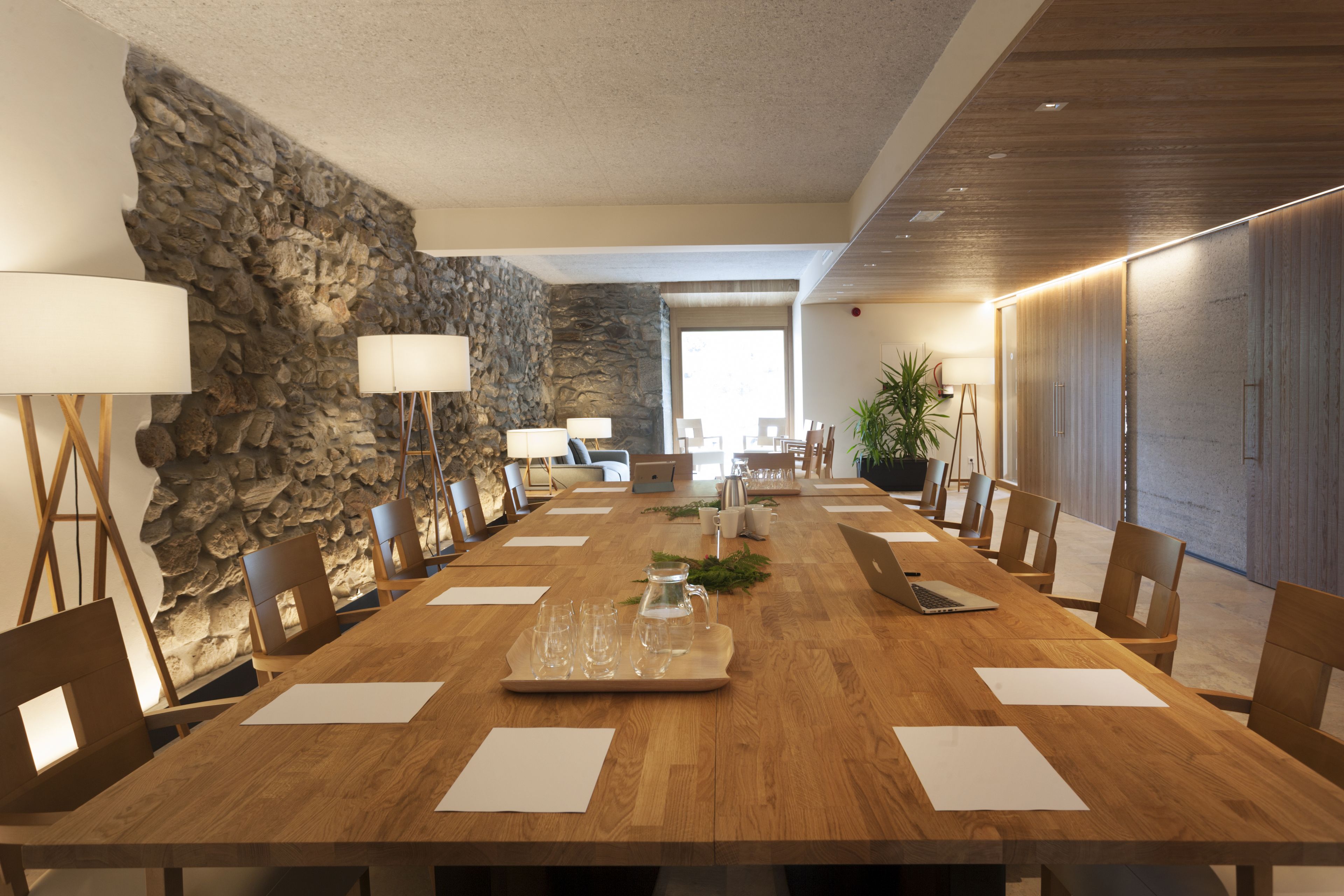 Un salón de conferencias con una larga mesa de madera, sillas y una pared de piedra.