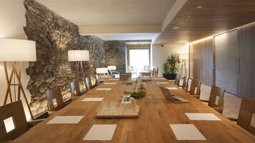 Un salón de conferencias con una larga mesa de madera, sillas y una pared de piedra.