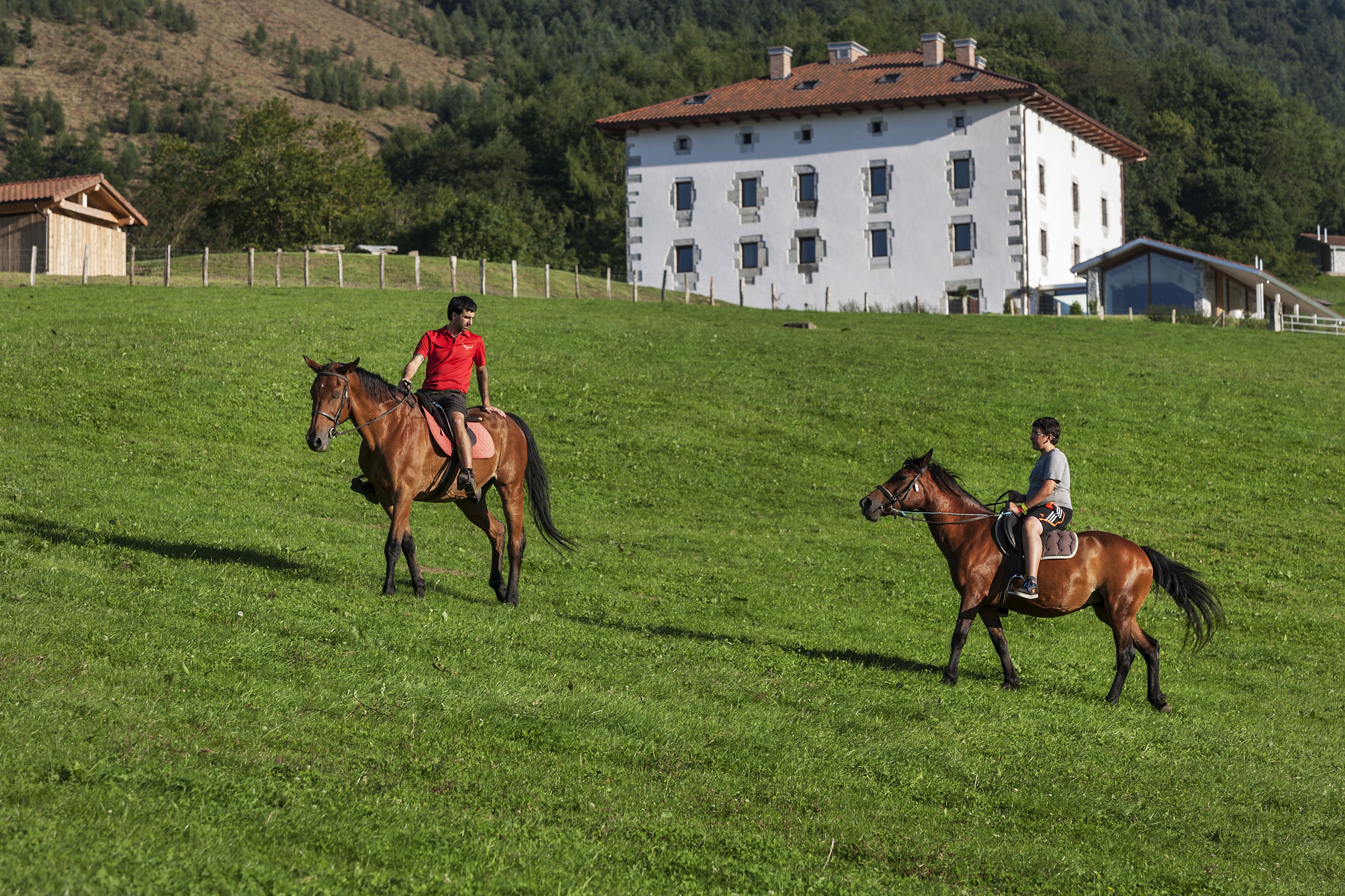 Two people riding horses on a grassy field with a large white building in the background.