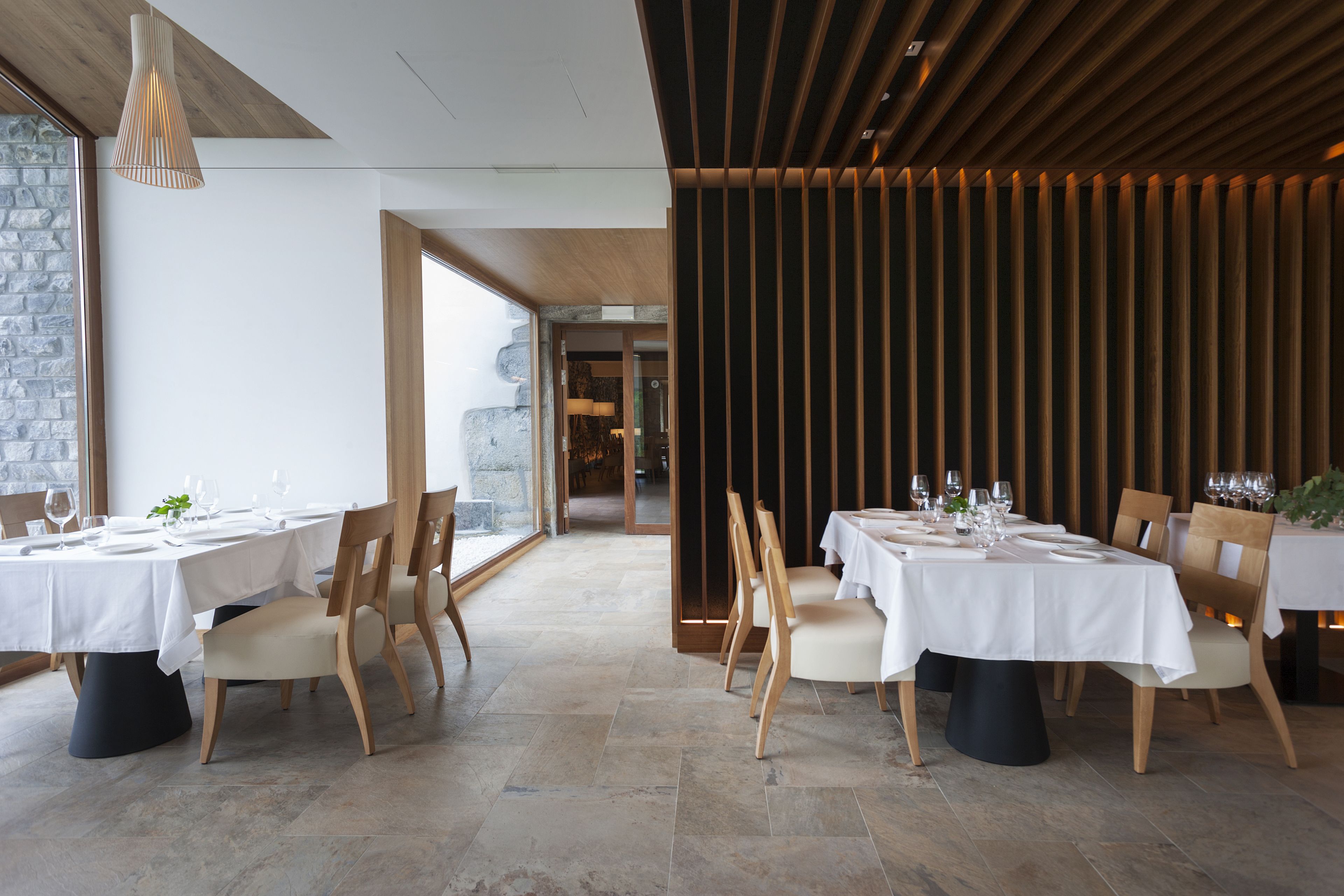 A restaurant with multiple tables set for dining, wooden chairs, and a modern interior design.
