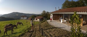 Un bâtiment avec un toit recouvert de tuiles rouges, un chemin de gravier et une zone herbeuse où se trouvent des chevaux.