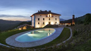 A large house with a swimming pool, surrounded by a hilly landscape.