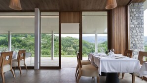 A dining area with a table set for four, wooden chairs, and a view of a lush landscape through large glass doors.