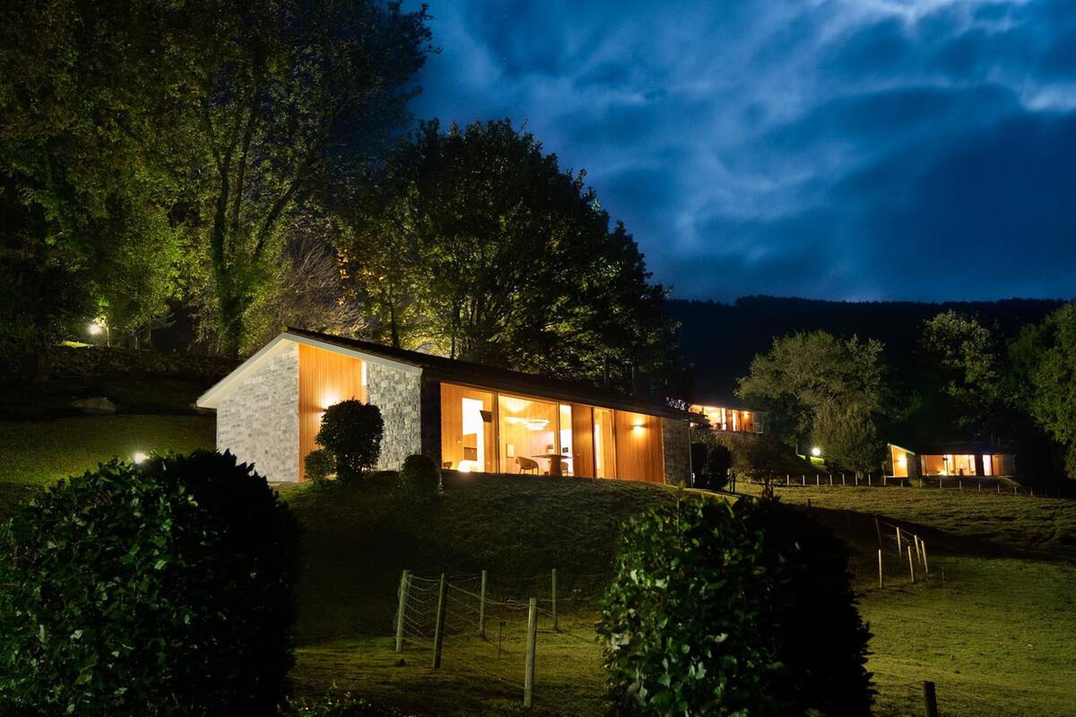 Une maison moderne avec une façade en pierre, de grandes fenêtres et un intérieur bien éclairé.