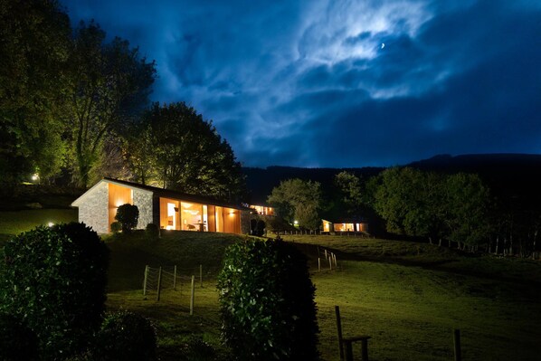 Une maison moderne avec une façade en pierre, des fenêtres illuminées et une pelouse bien entretenue.
