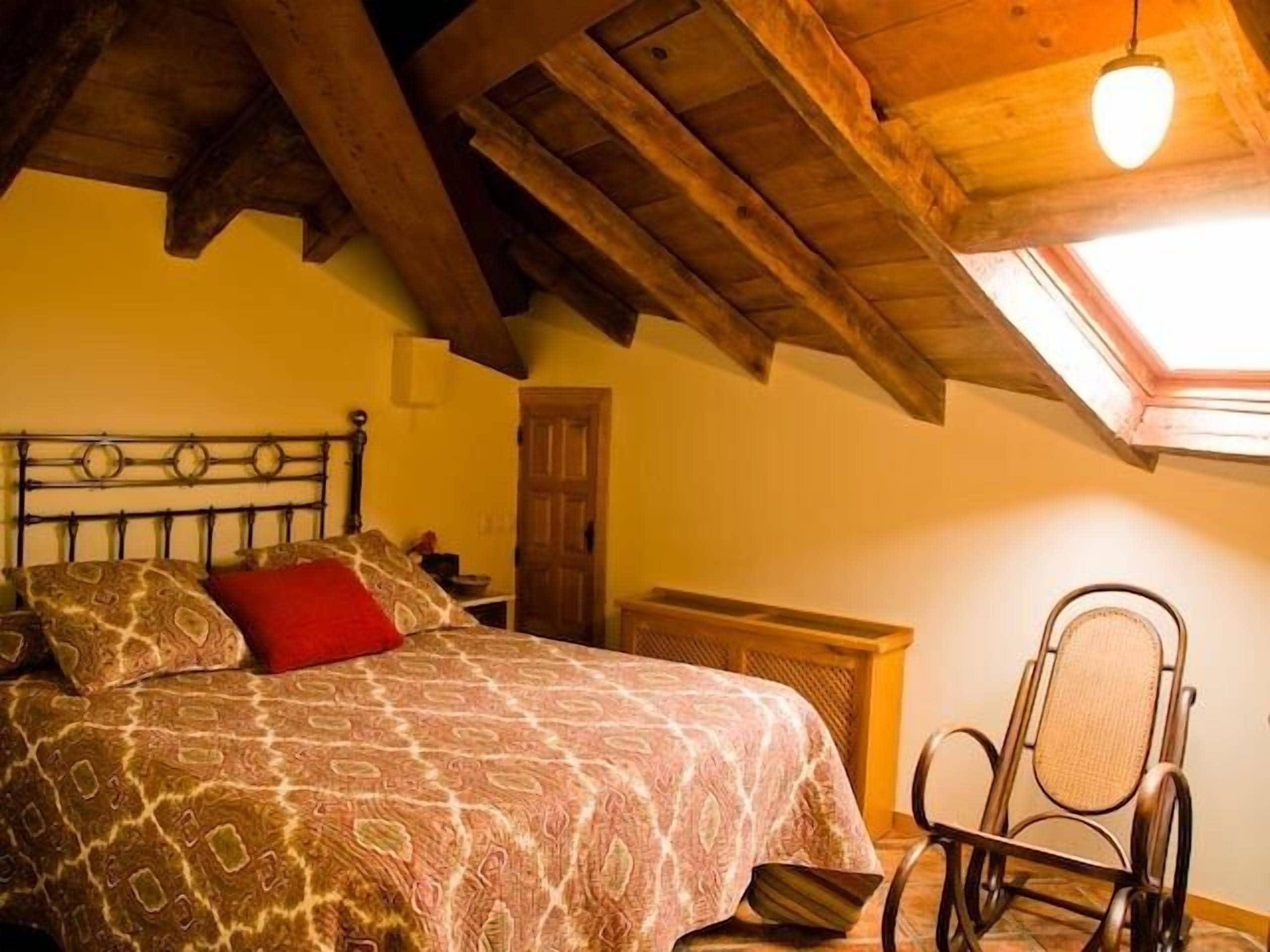 Une chambre à coucher avec un lit, une chaise, un bureau en bois et une lucarne.