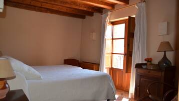 A bedroom with a bed, wooden headboard, a nightstand with a lamp, a wooden dresser, and a window with curtains.