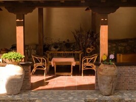 Un patio al aire libre con una mesa y sillas de madera, rodeado de macetas grandes con flores.