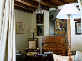 Una habitación tradicional con techo de madera, un candelabro, un sillón floral, un aparador de madera y obras de arte enmarcadas en las paredes.