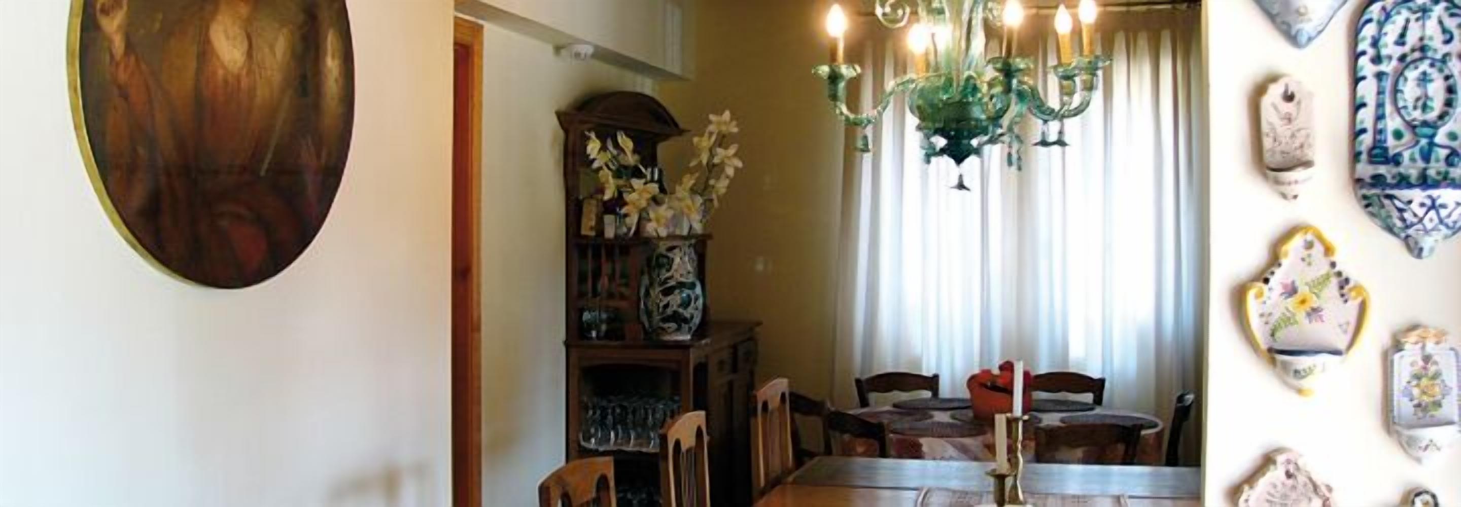 A dining area with a chandelier, wooden chairs, a table, and a vase of flowers on a shelf.