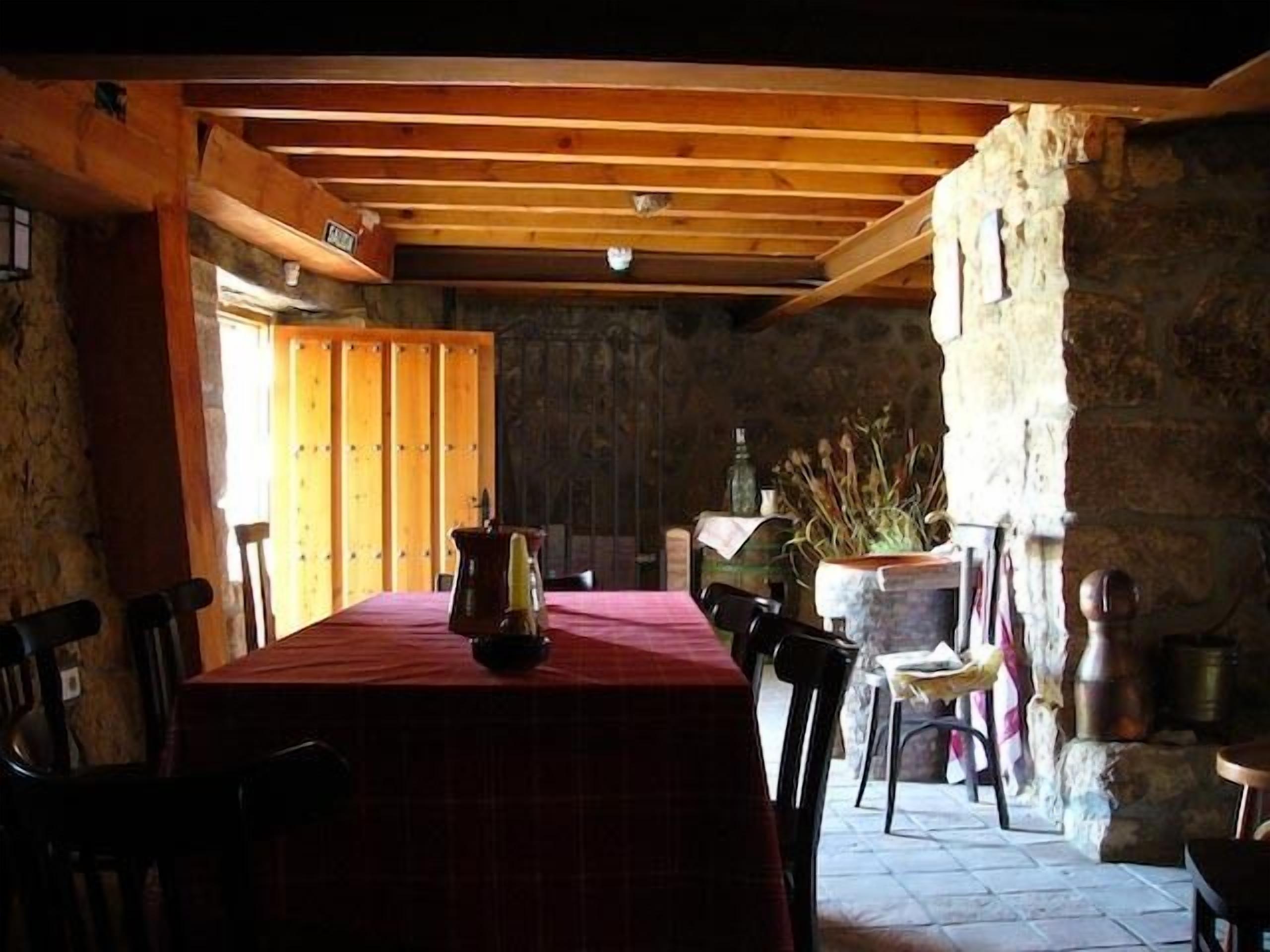Zona de menjador rústica amb taula i cadires de fusta, paret de pedra i una planta en test.