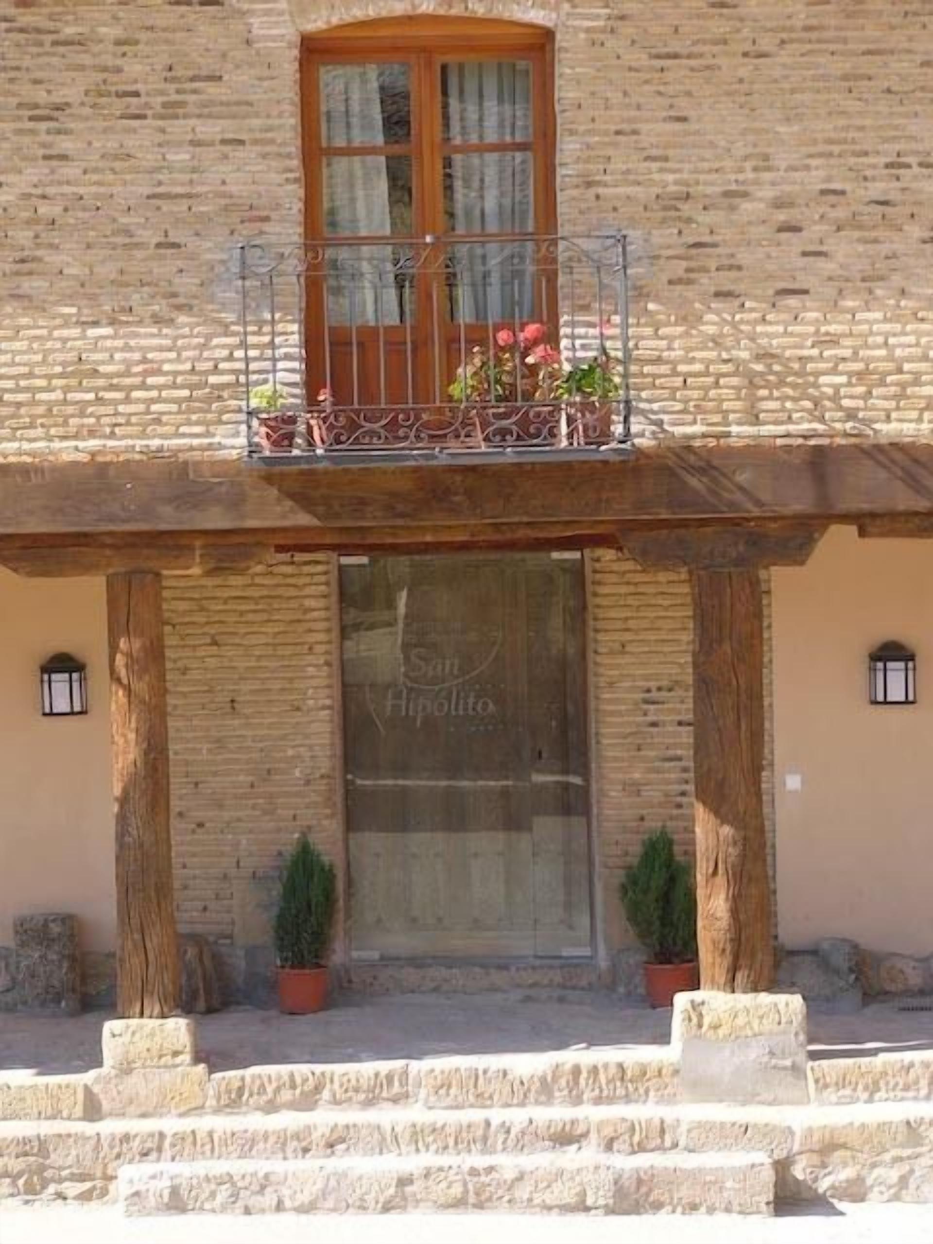 A building with a stone facade, a wooden balcony with a wrought iron railing, and a large window with the inscription "San Hipolito".
