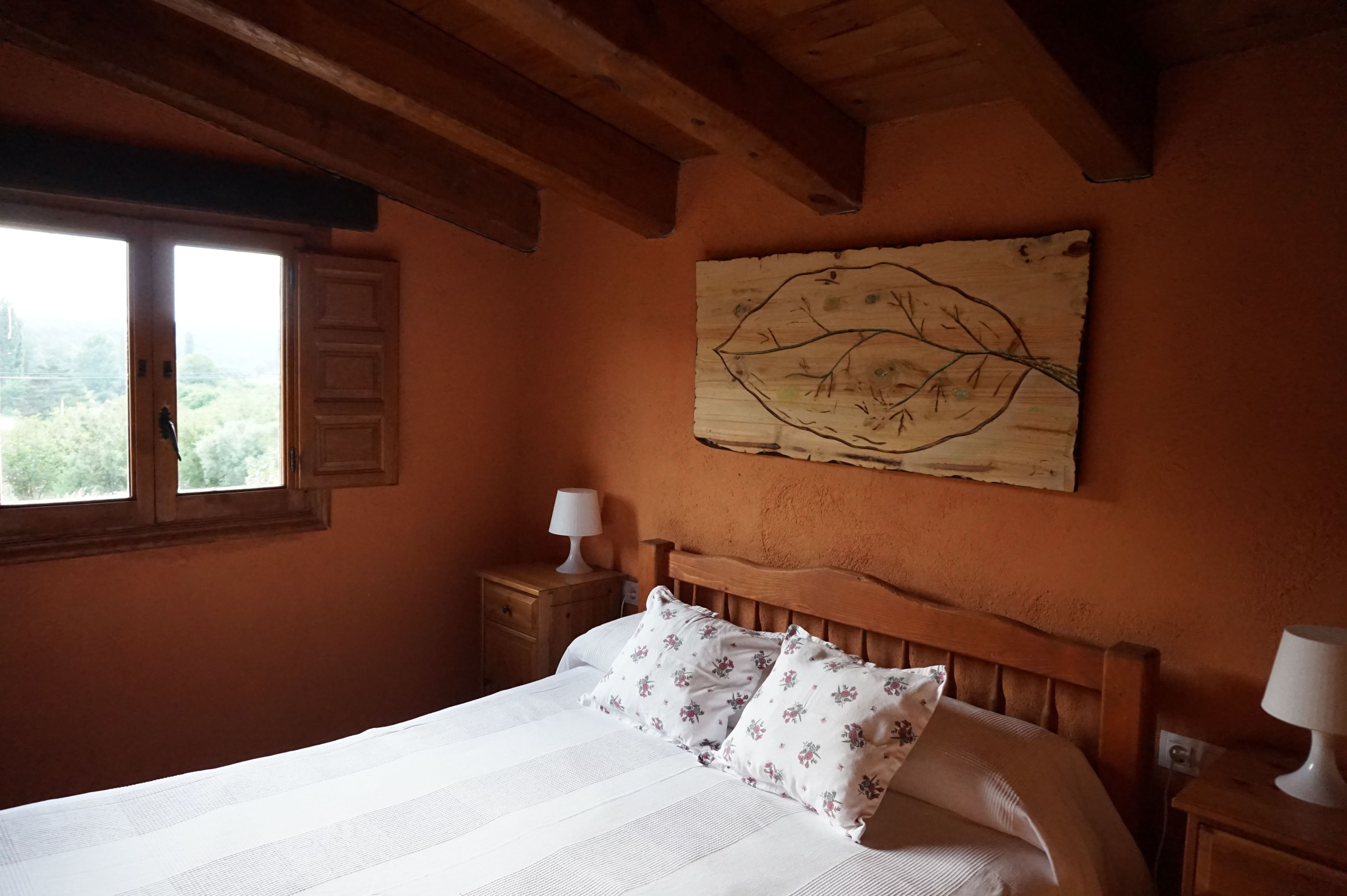 Quarto com cama de madeira, mesa de cabeceira, luminária na parede e janela com persianas.