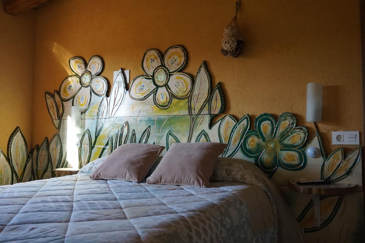 A bedroom with a bed, pillows, a nightstand, and a wall decoration.