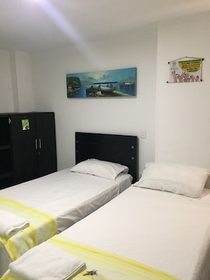 Ein Zimmer mit zwei Einzelbetten, einem dunklen Kopfteil, einem Bild von Booten auf dem Wasser und einem Poster an der Wand.
