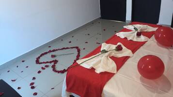Een kamer met een bed bekleed met een rood-witte deken, een rode roos en rode ballonnen.