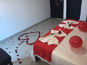 Ein Zimmer mit einem Bett, das mit einer rot-weißen Decke, einer roten Rose und roten Luftballons dekoriert ist.