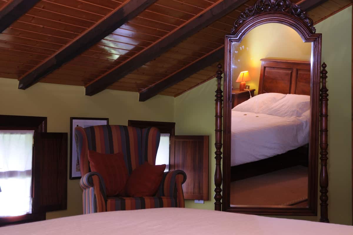 Quarto com um espelho grande, uma cama, uma poltrona listrada e teto de madeira.