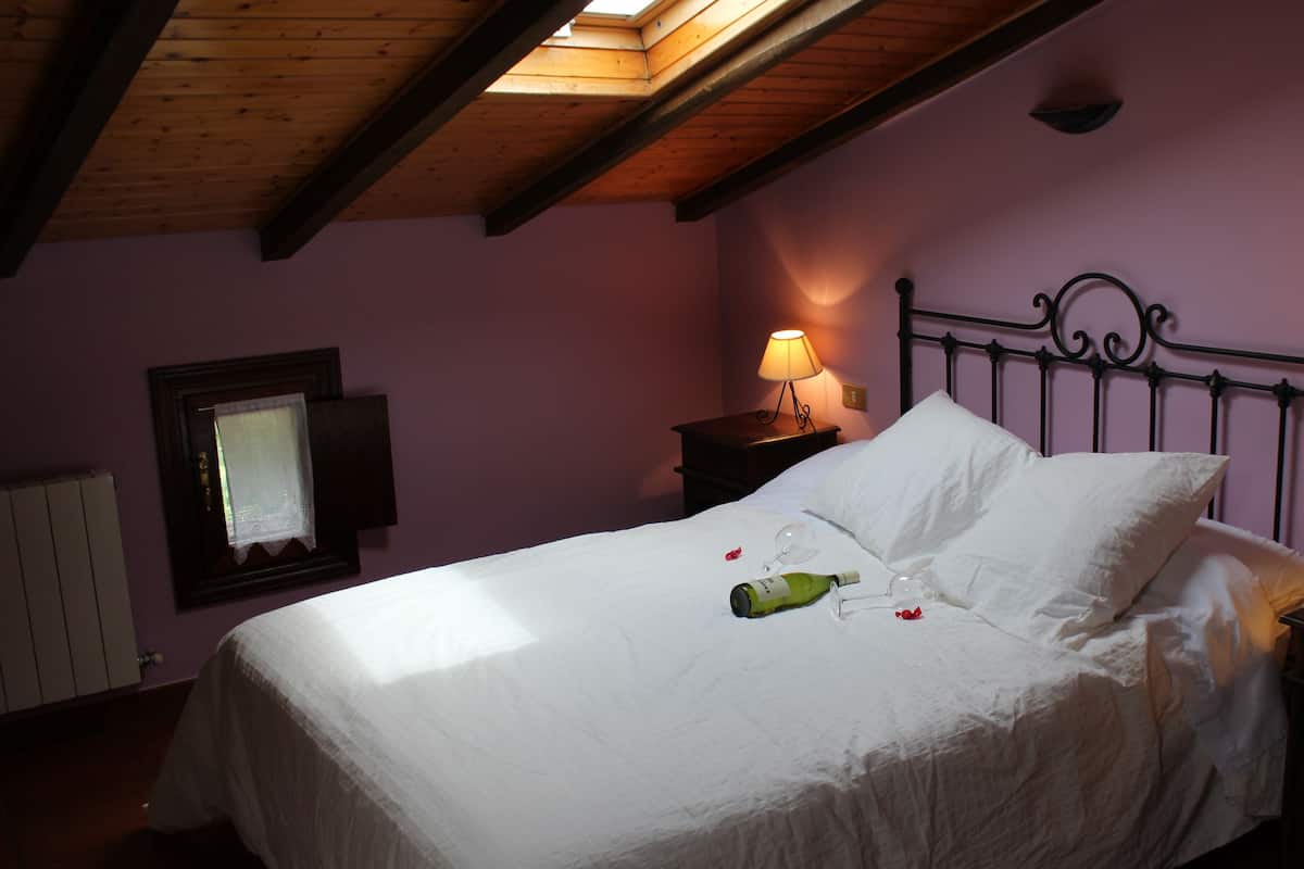 Quarto com cama, duas luminárias de cabeceira, janela com cortina e teto de madeira.