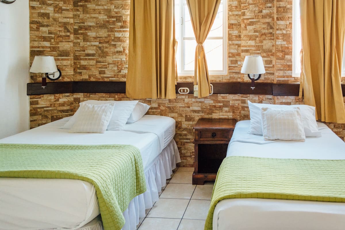 Habitación de hotel con dos camas, una pared de ladrillo y una ventana con cortinas.