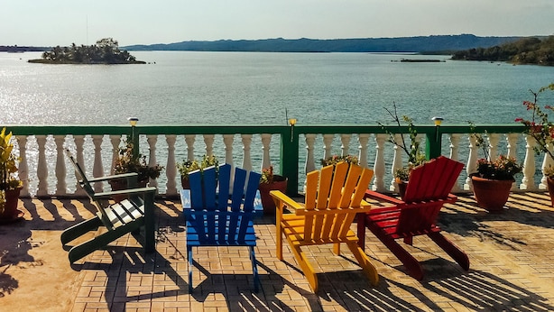 Una terraza con vistas a un lago, con tres sillas Adirondack y plantas en macetas.
