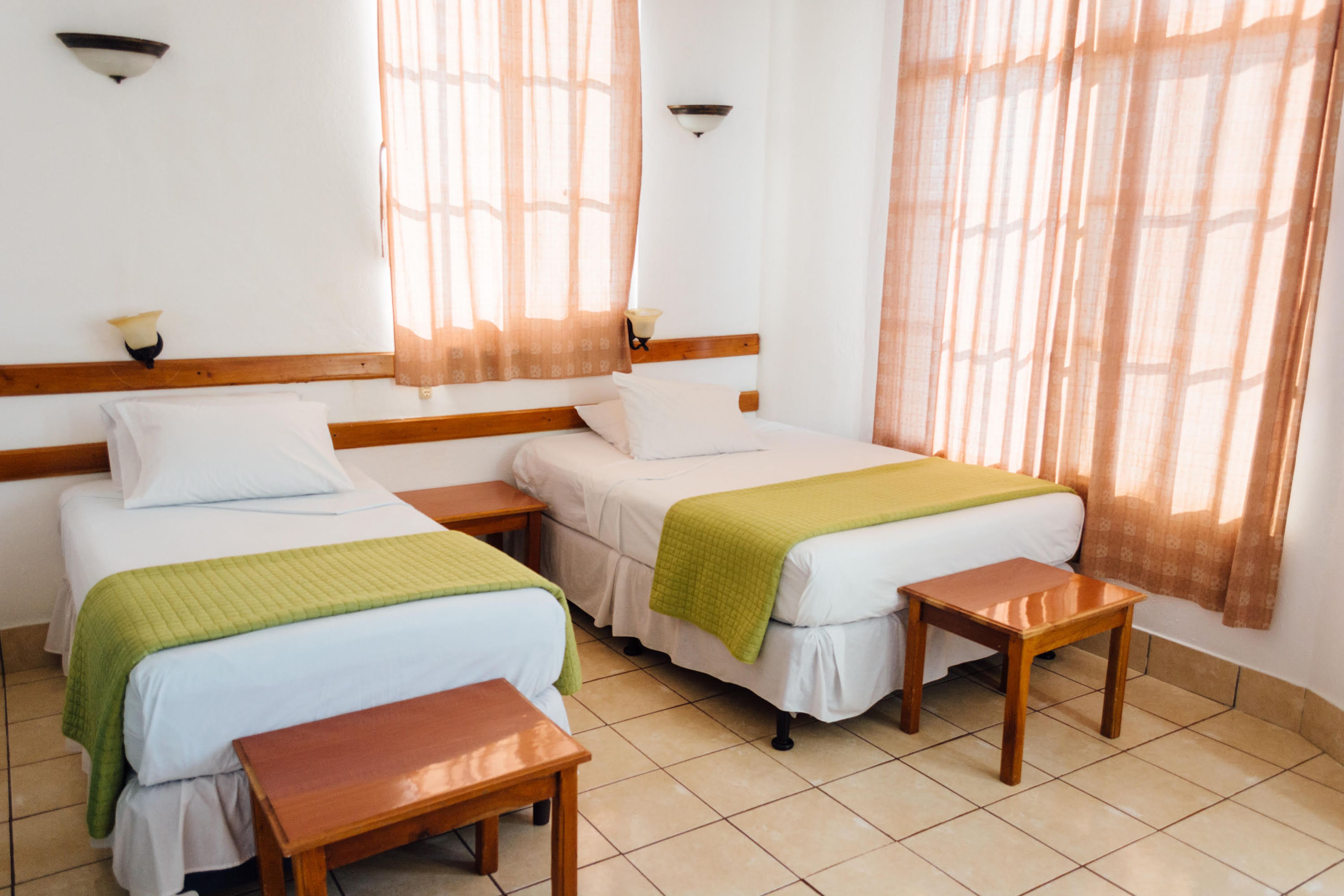 Una habitación de hotel con dos camas individuales, cabeceros de madera, una mesita pequeña y un banco.