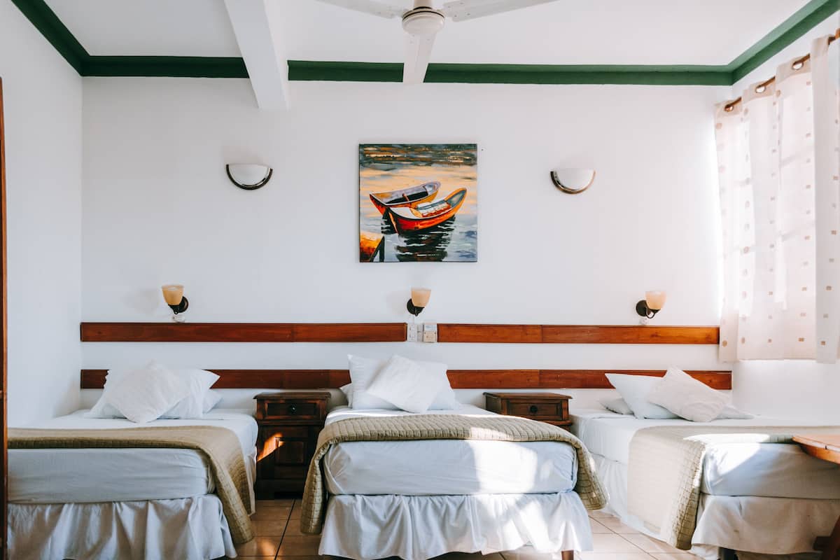 Habitación de hotel con dos camas, cabecera de madera, un cuadro de un barco y dos lámparas de pared.