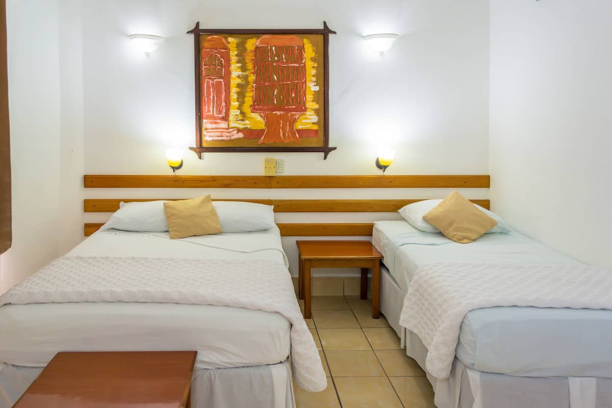 Habitación de hotel con dos camas individuales, cabecero de madera, una mesita pequeña y una obra de arte colgada en la pared.