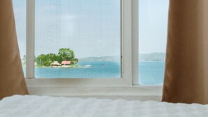 Una habitación con un amplio ventanal que da a una masa de agua y una costa distante con edificios y vegetación.