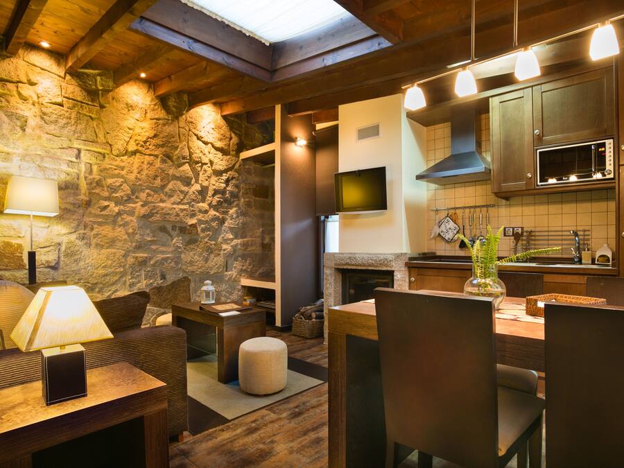 A cozy kitchen with stone walls, wooden beams, a flat-screen TV, and a modern microwave.