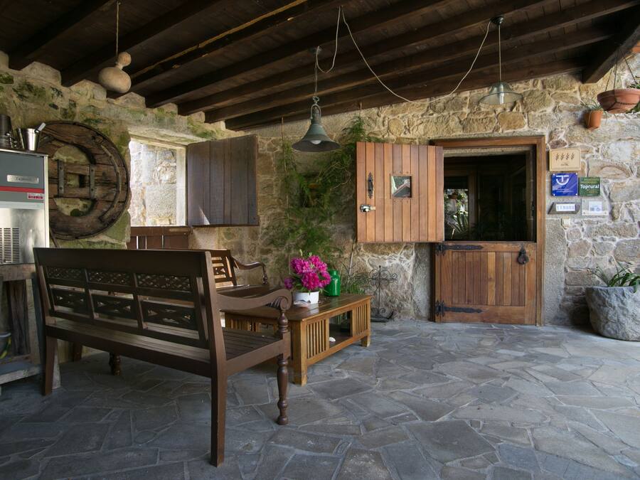 A rustic stone-walled room with a wooden bench, a small table with a vase of flowers, and a wooden door.