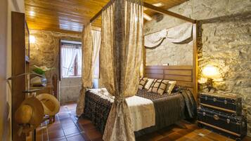Une chambre à coucher rustique avec un mur en pierre, un plafond en bois, un lit avec une literie à motifs, une lampe de chevet et une valise.