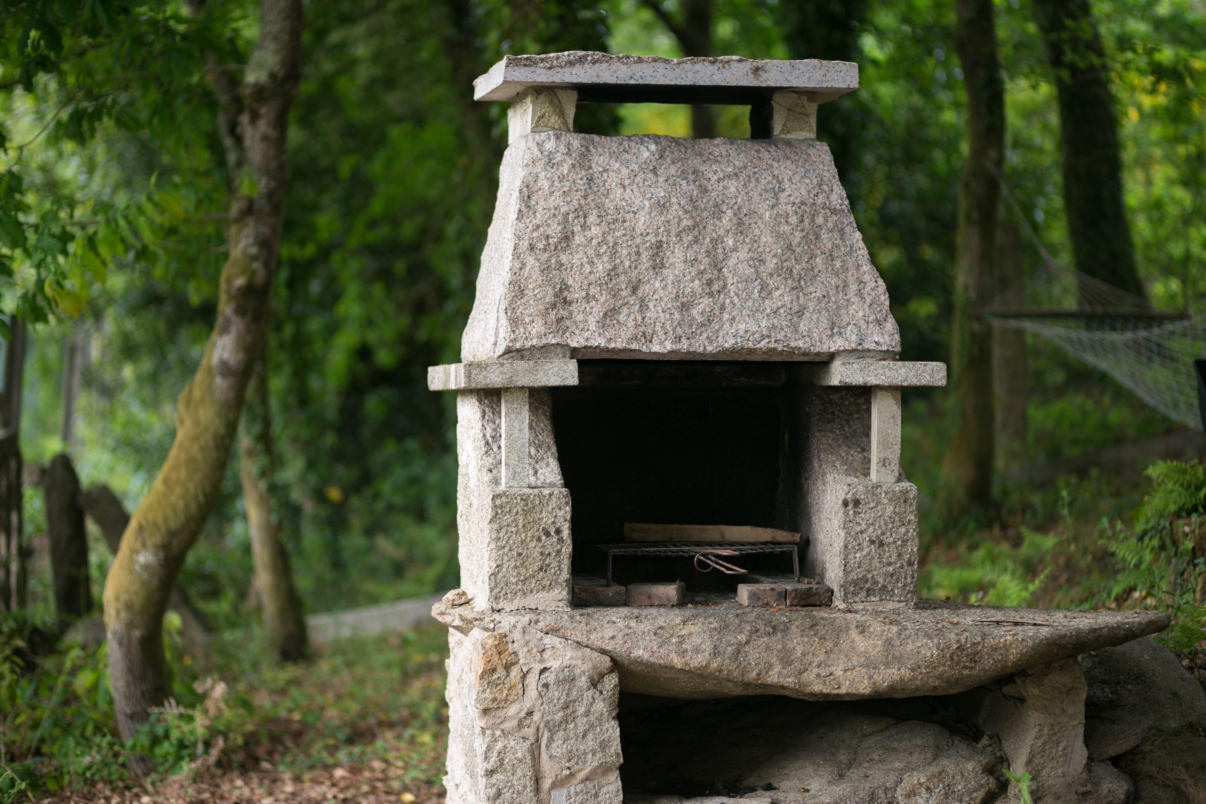 A stone-built outdoor fireplace in a forested area.