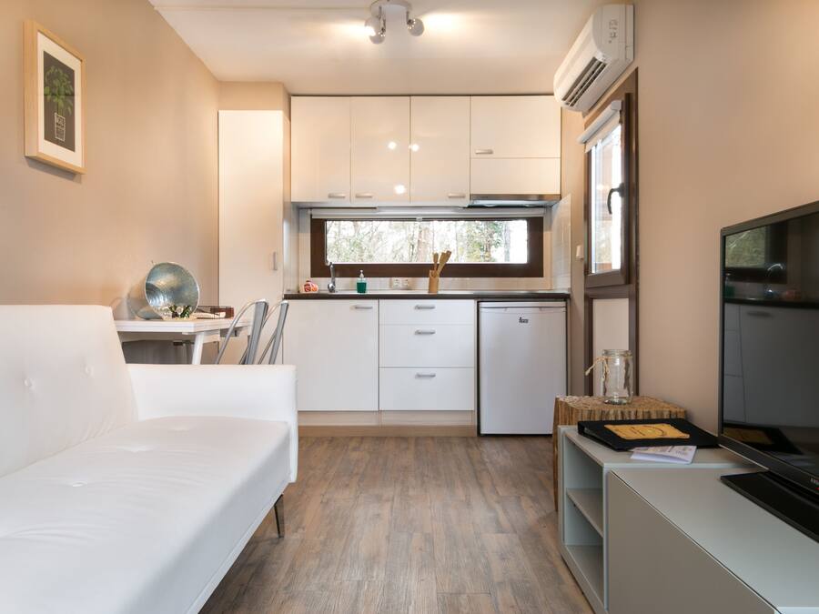 Un espacio habitable compacto con kitchenette, un sofá, un televisor de pantalla plana y un ventanal que proporciona luz natural.