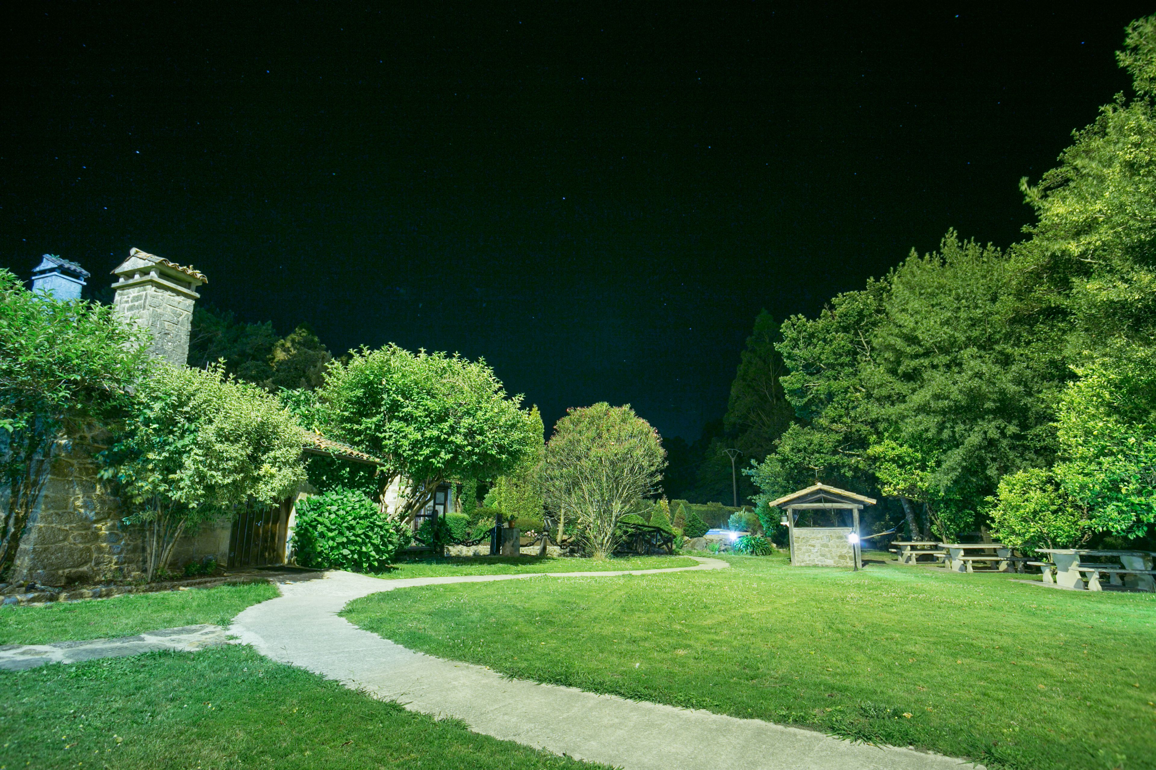 Vista nocturna de un parque con sendero pavimentado, estructuras de piedra y mesas de picnic.