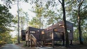 A modern wooden cabin with a deck and stairs, surrounded by trees. - Aldea Os Muiños (Rianxo)