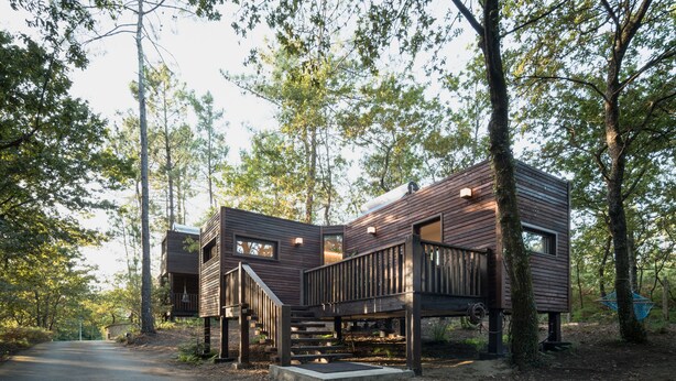A modern wooden cabin with a deck and stairs, surrounded by trees. - Aldea Os Muiños (Rianxo)
