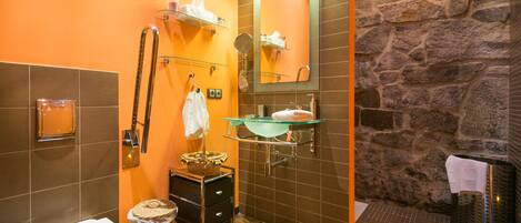 Un baño con pared de piedra, lavamanos de vidrio, espejo, toallero y retrete.