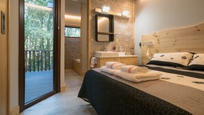 A modern bedroom with a large bed, a wooden headboard, a built-in sink, and a balcony with a view of trees. - Aldea Os Muiños (Rianxo)