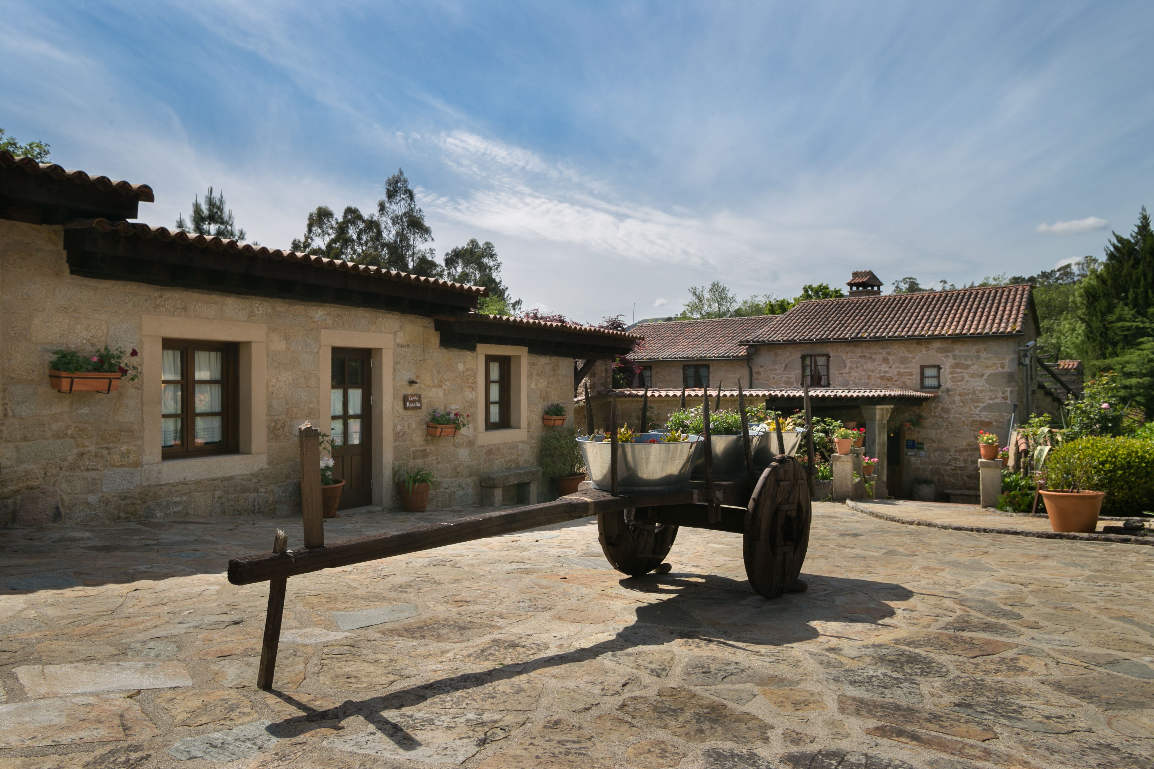 A stone building with a rustic exterior, a cart in front, and potted plants around.