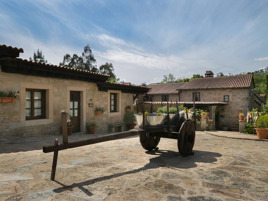 A stone building with a rustic exterior, a cart in front, and potted plants around.