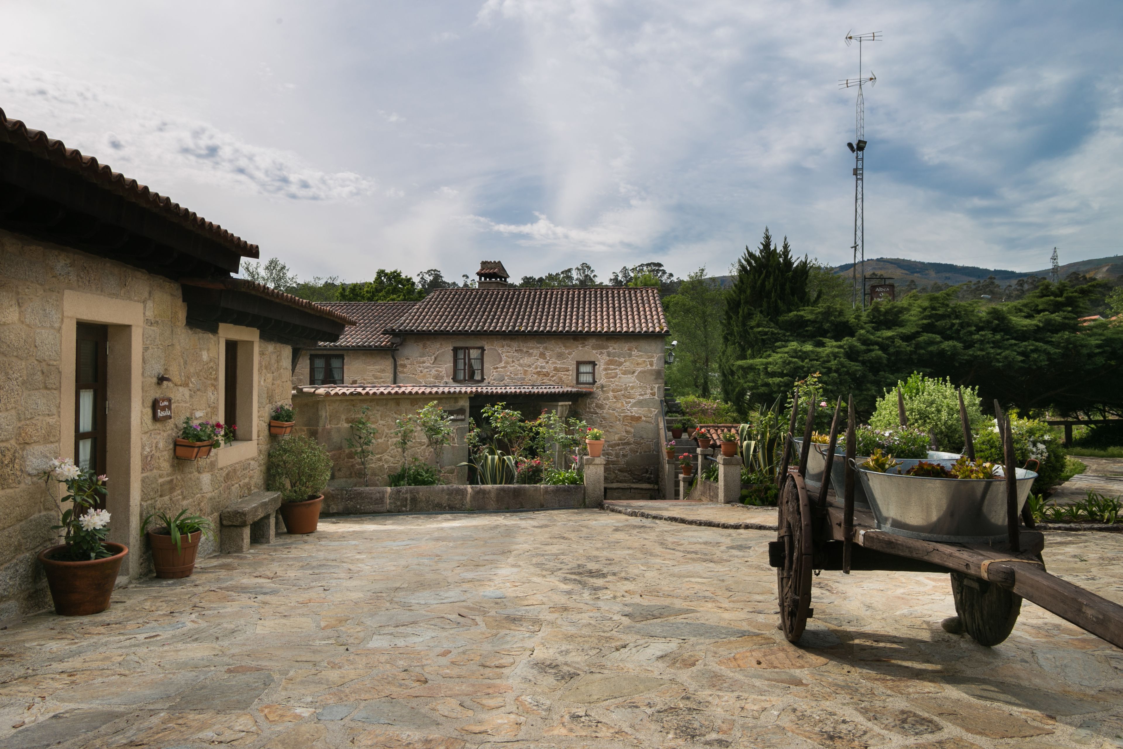 A stone building with a tiled roof, potted plants, and a cart with a metal container.